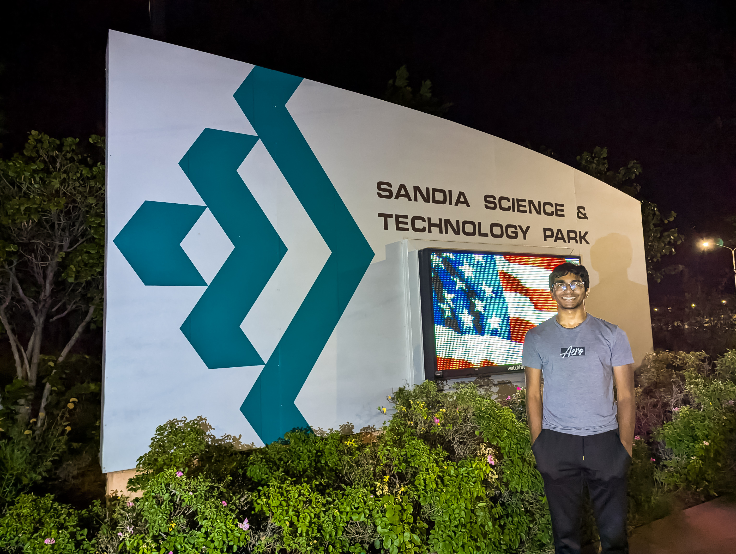 Saha standing in front of a large sign that says "Sandia Science and Technology Park"