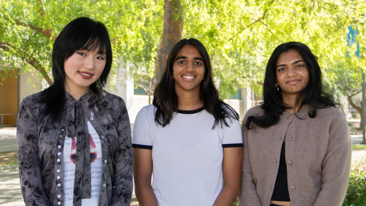 Zhou, Rajput, and Mohan stand together outdoors, smiling, with trees in the background.
