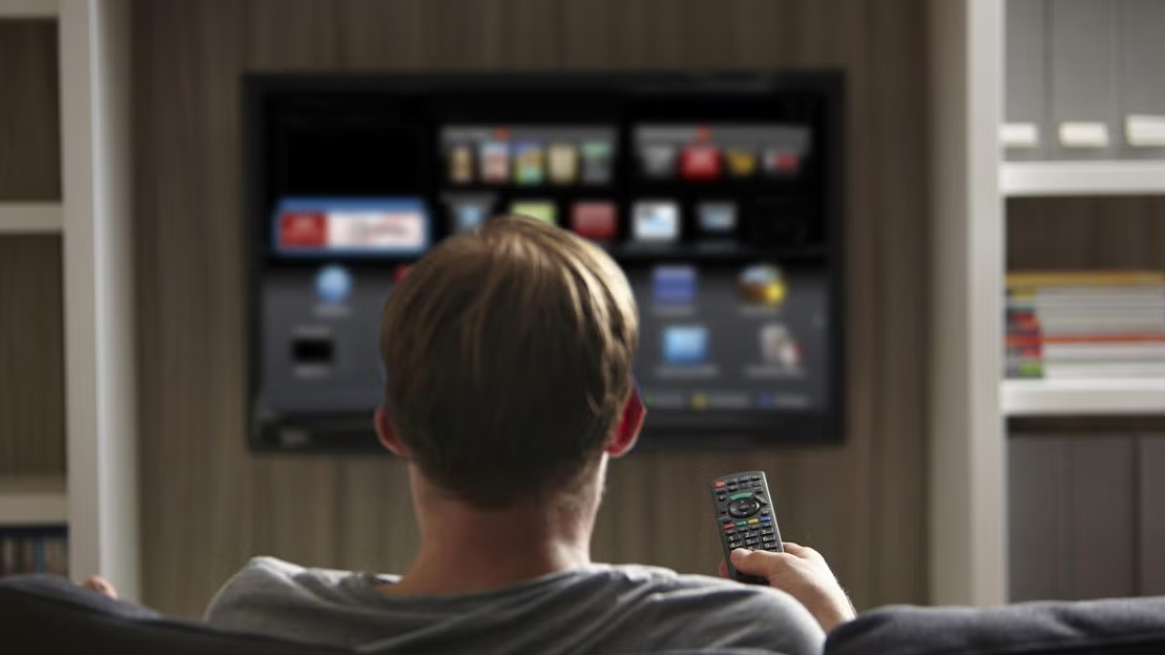 Back of someone's head as they hold a remote and look at a smart TV mounted to the wall