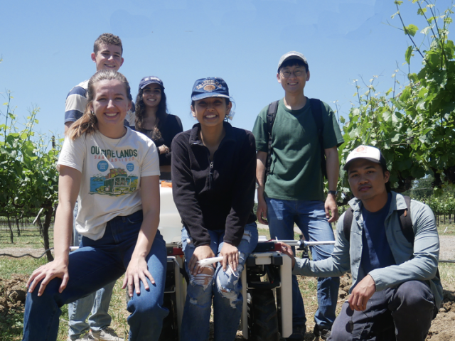 Students stand in field with a robot