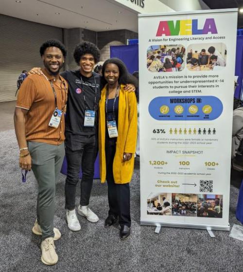 Three people posing for a photo next to a stand-up banner that says AVELA