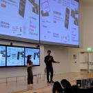 Two students speaking into microphones in front of giant screens