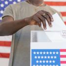 Person places ballot in box, American flags are seen on the box and in the background